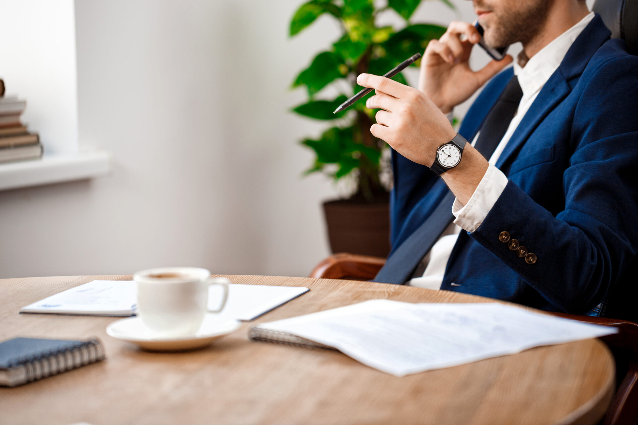 Close up of young successful businessman speaking on phone at workplace, office background.